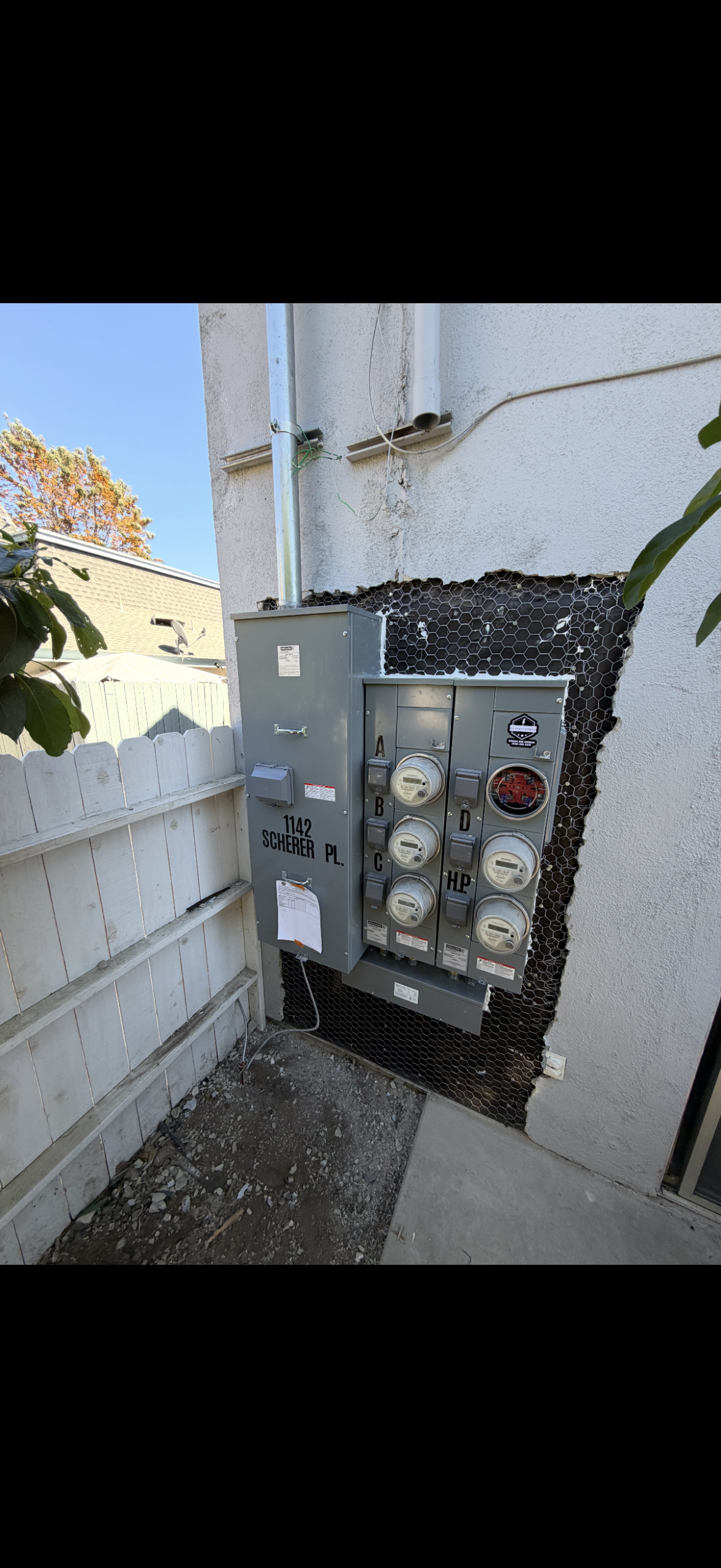 Four electric utility meters and a gray service panel are mounted on an exterior wall, with exposed wiring around the installation area. Address: 1142 Scherer Pl.